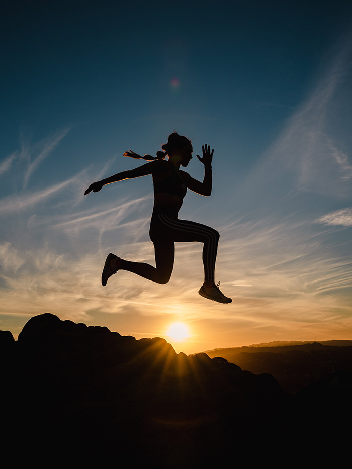 woman with long hair jumping with the sun setting behind her